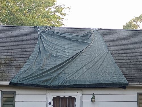 Blue tarp covering damage on a house roof after a storm
