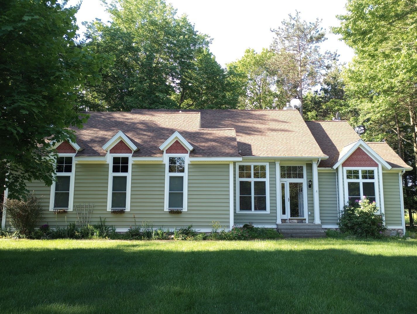 Small beige house with white trim and dormer windows, set behind a grassy lawn and trees.