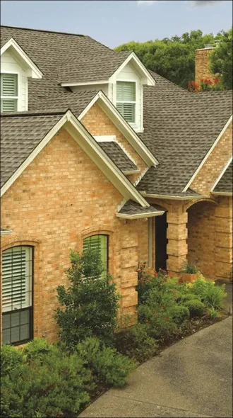 Brick suburban house with gray shingled roof, white trim, and landscaped front shrubs