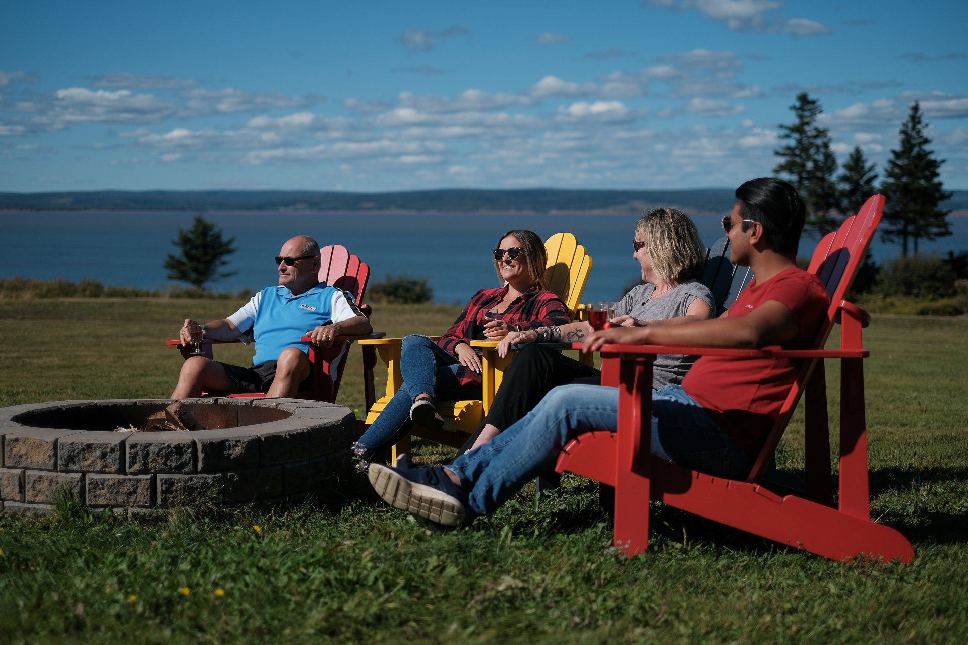 people sitting next to a fire pit with the bay of fundy in the background