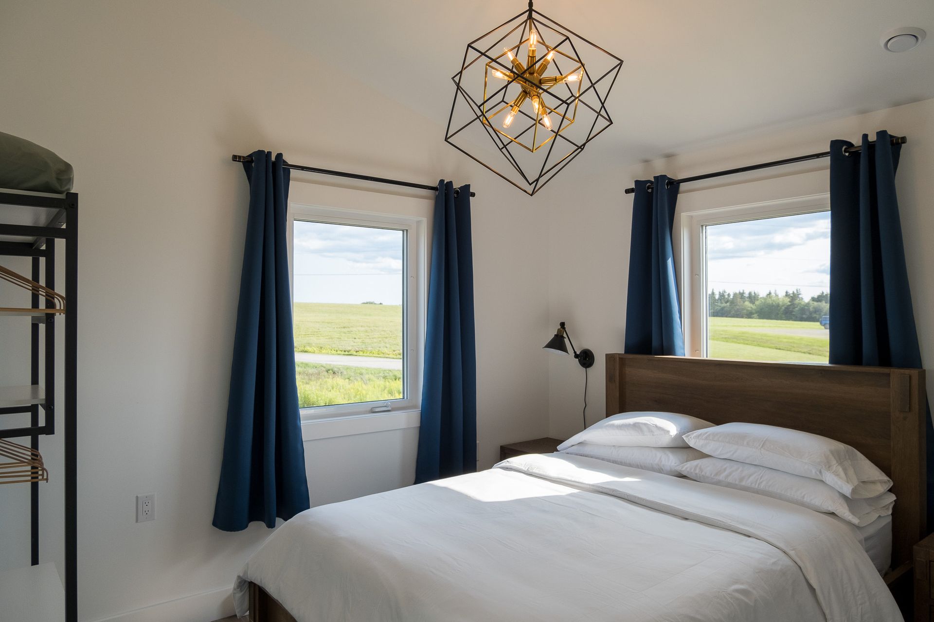 queen bed in the centre of a bedroom with a vaulted ceiling, chandelier, and large windows that frame beautiful grassy field