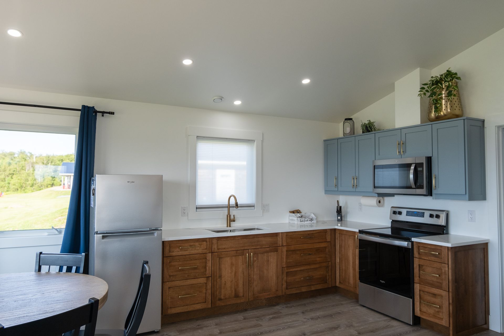 Cottage kitchen area, with fridge, sink under the window, stove, oven, microwave, cupboards, and a kitchen table.