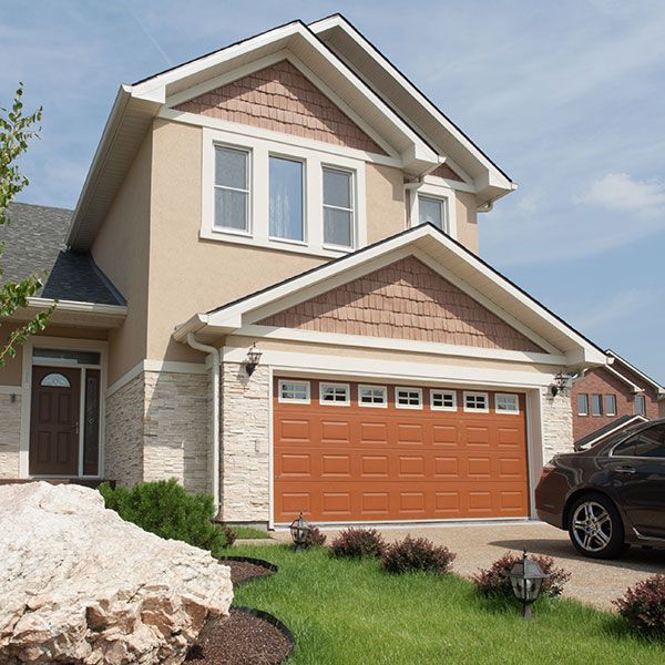 Suburban house with beige siding, stone accents, and a double garage with an orange door.