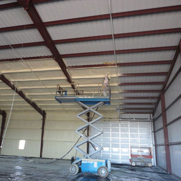 man on scissor lift installing spray foam in metal building