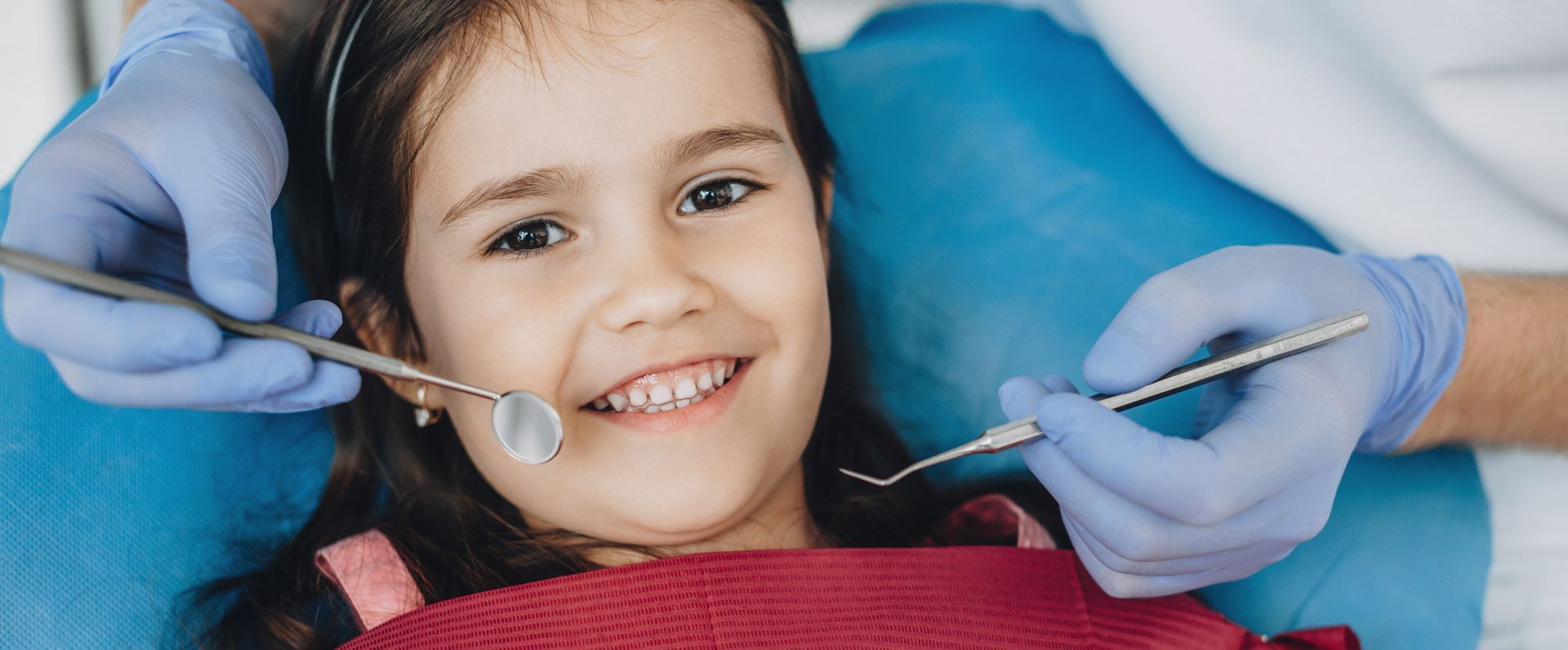 Child receiving a dental checkup while a dentist uses a mirror and dental explorer.