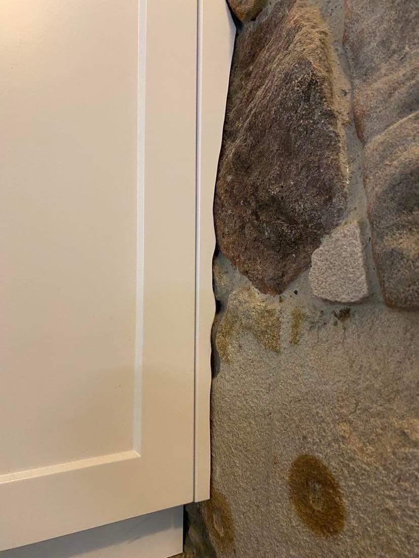 A White Cabinet Edge Installed Against a Rough, Textured Stone Wall — Craftsmen Kitchens In Monkland, QLD