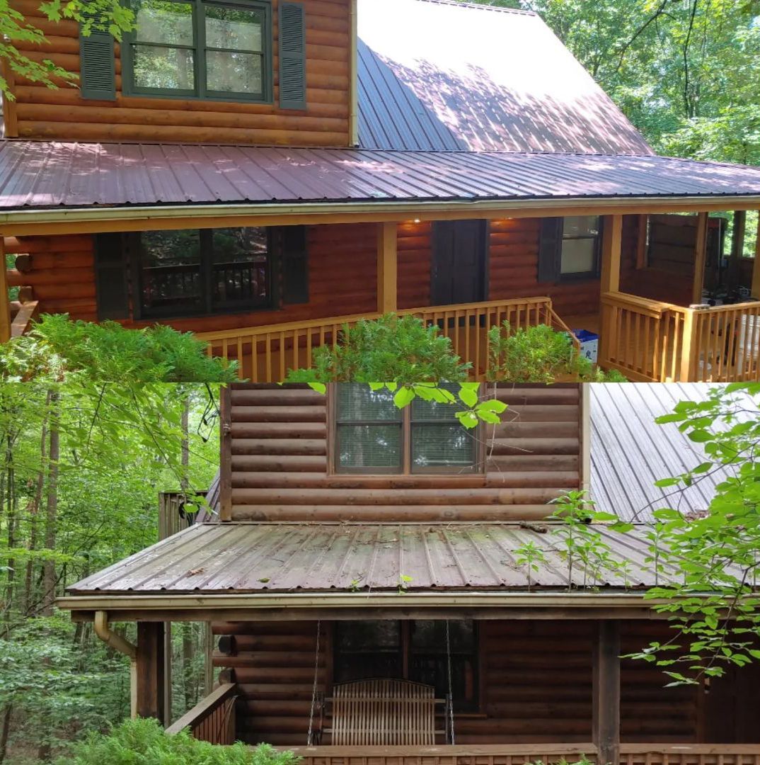 Two-story log cabin with a red metal roof and a wooden porch in a wooded setting.