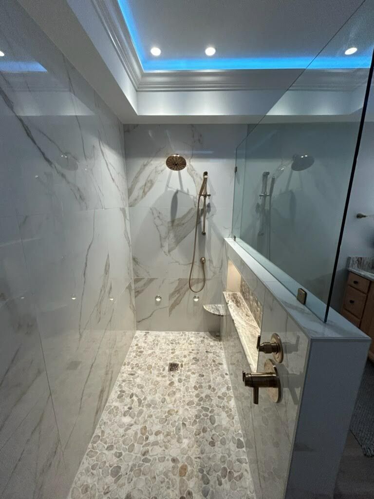 Elegant marble and glass shower with gold fixtures, pebble floor, and accent lighting.