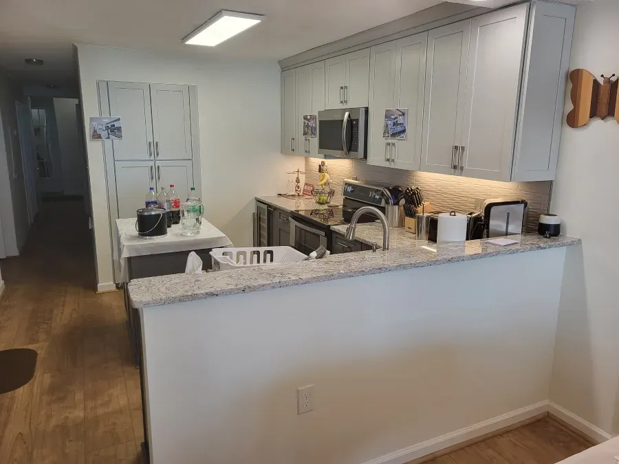 A small kitchen with light-colored cabinets, a countertop, a sink, and appliances. A doorway leads to a hallway.