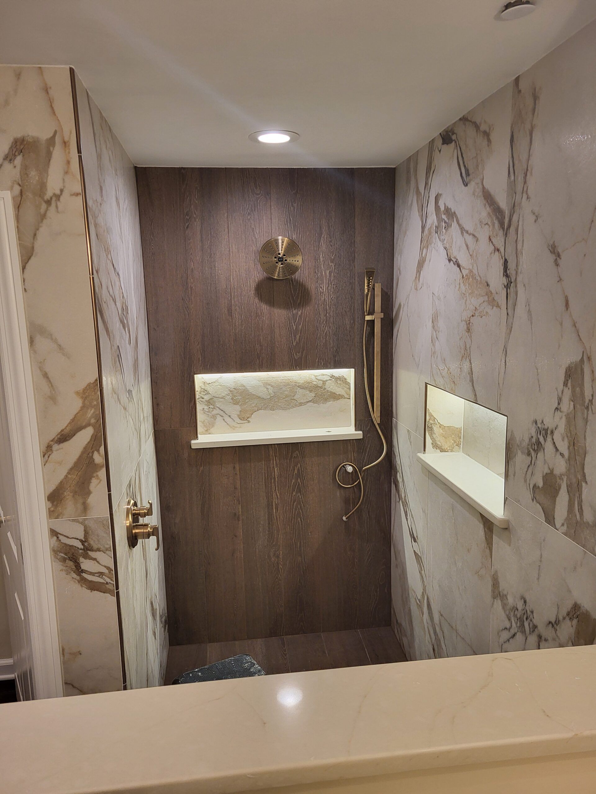 A luxurious shower with marble walls and a dark brown accent wall, gold fixtures, and built-in shelves.