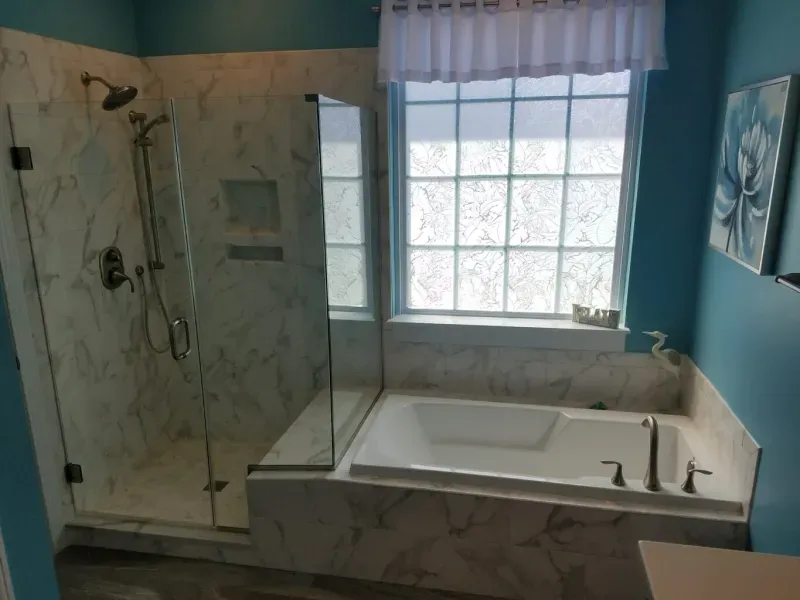 Bathroom with marble-patterned shower and bathtub, teal walls, and a window with a frosted privacy film.