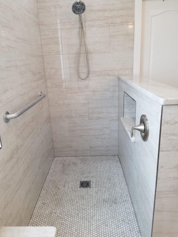 A modern, accessible shower with light-colored tile walls, a tiled floor, a grab bar, and built-in bench.