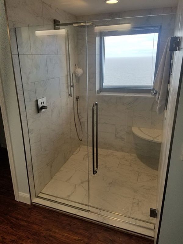 A modern shower with clear glass doors, marble-like tile, and a small window. A towel hangs on the side.