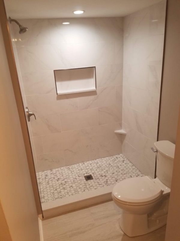 A newly renovated bathroom with a tiled shower, a toilet, and a pebble-tiled shower floor. The walls are white and the space is well-lit.
