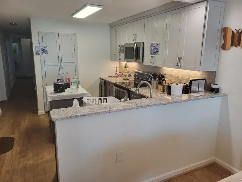A small kitchen with gray cabinets, granite countertops, and a partial wall. The kitchen has a microwave, sink, and a few appliances.
