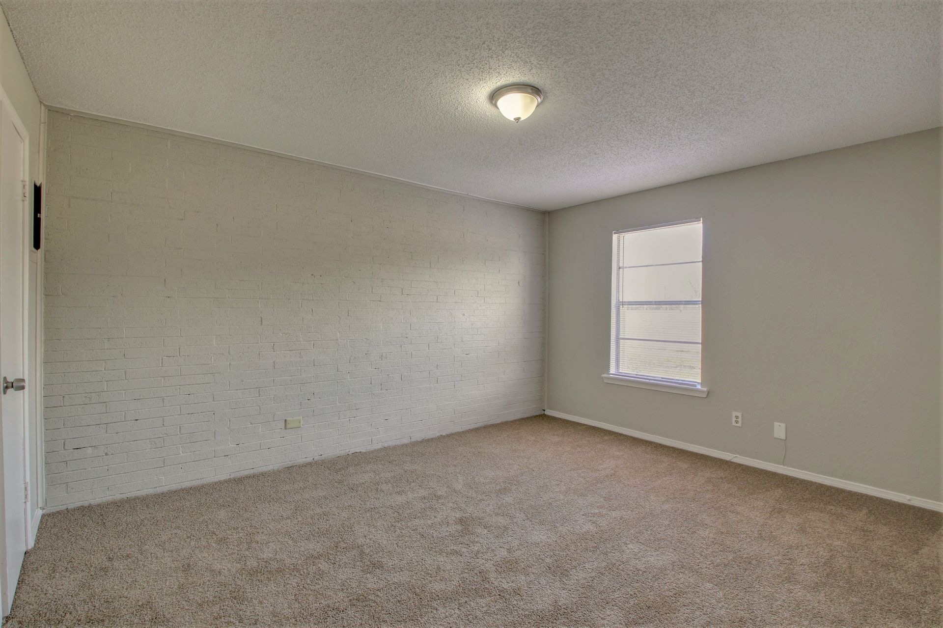 An empty bedroom with a window and a carpeted floor.