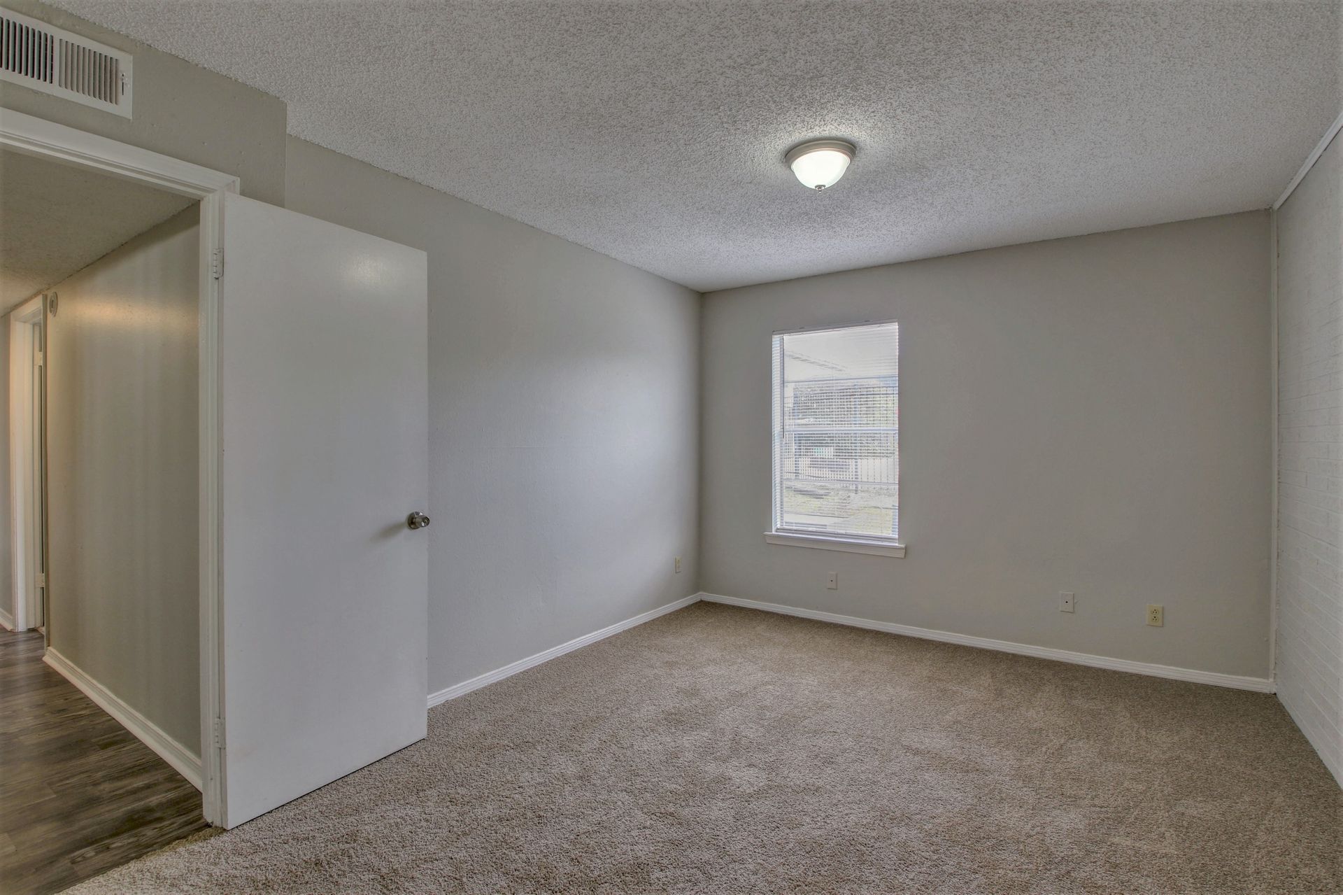 An empty bedroom with a window and a carpeted floor.