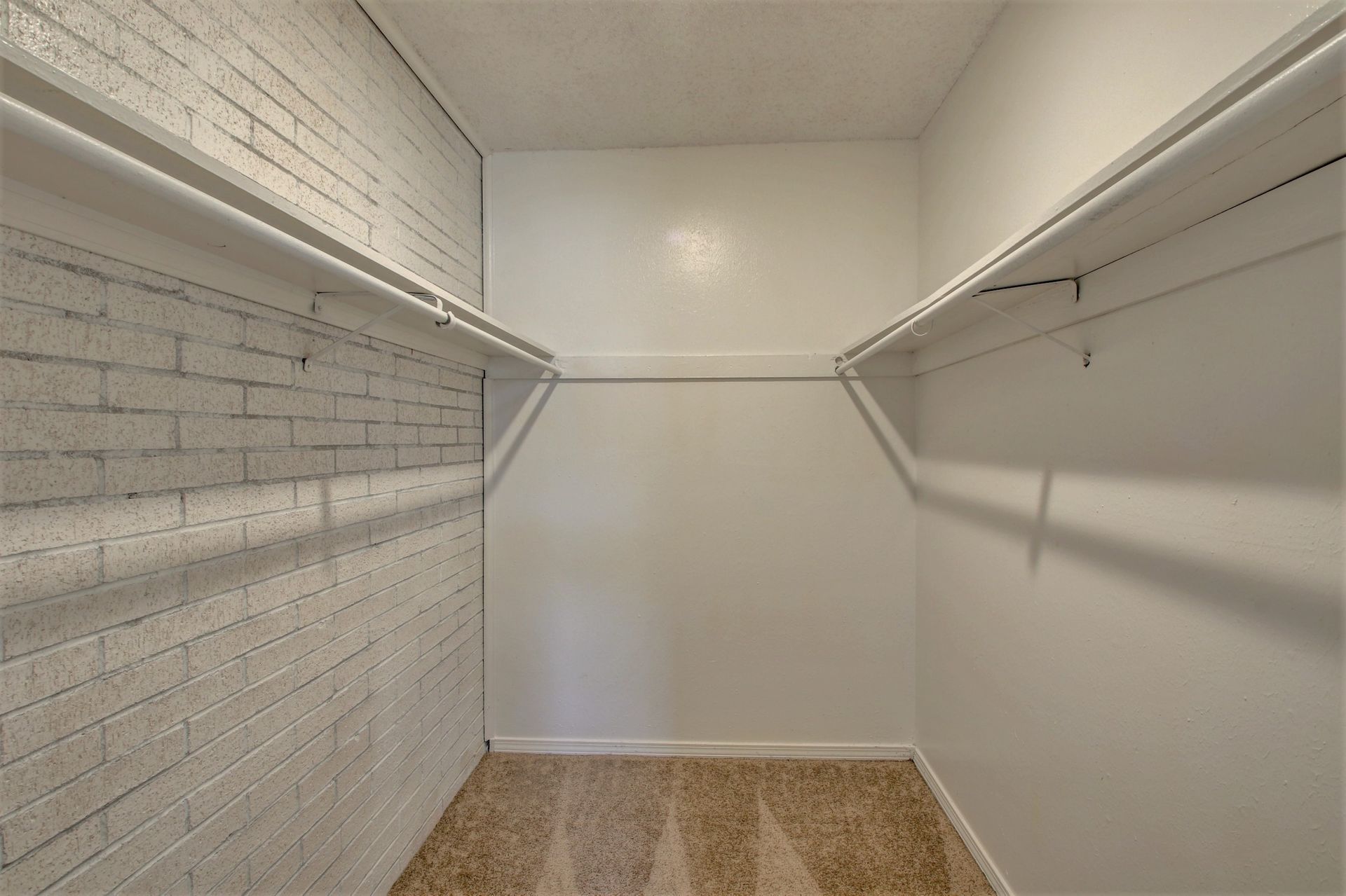 An empty walk in closet with a brick wall and white shelves.