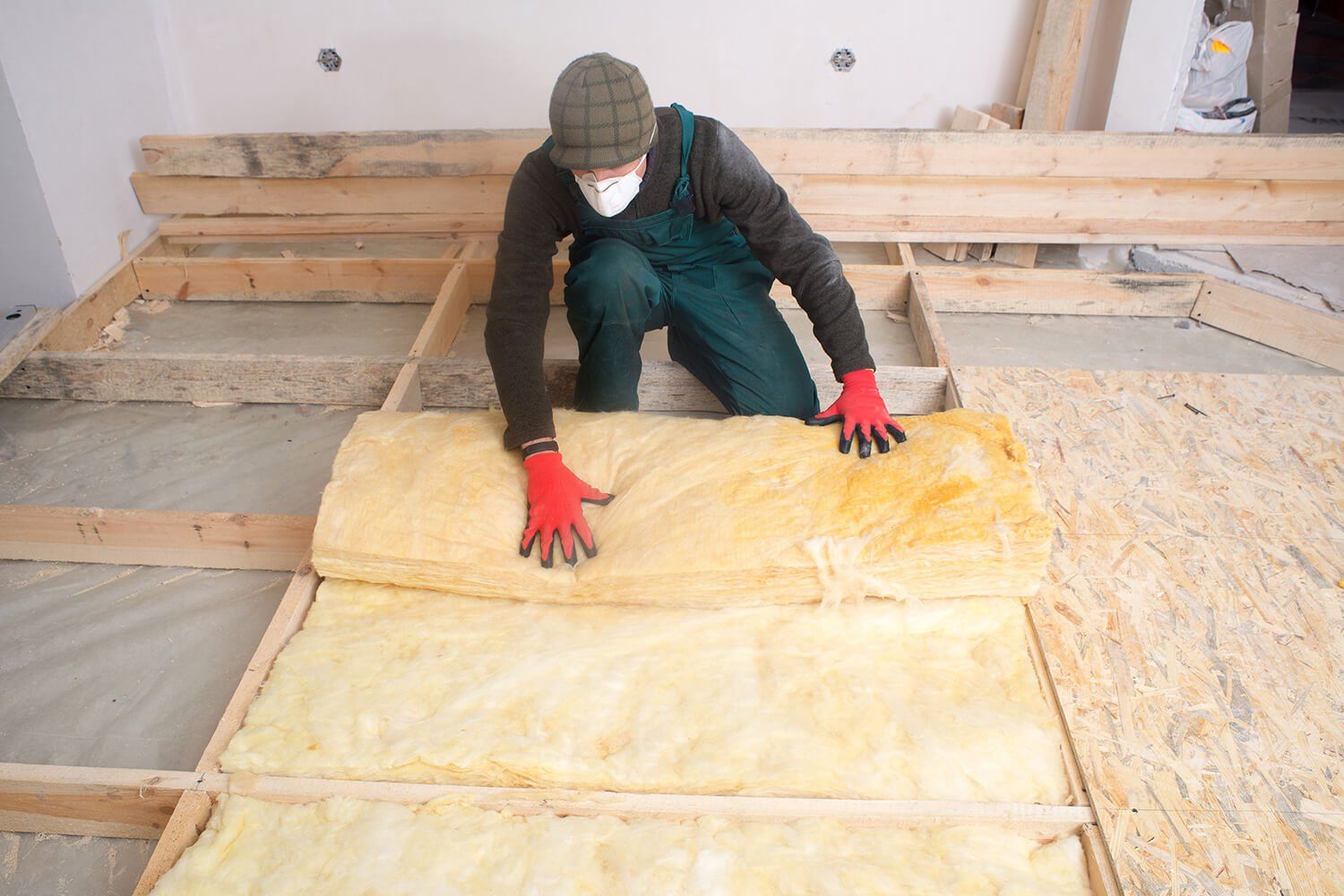 A man is laying underfloor insulation on a wooden floor joists.