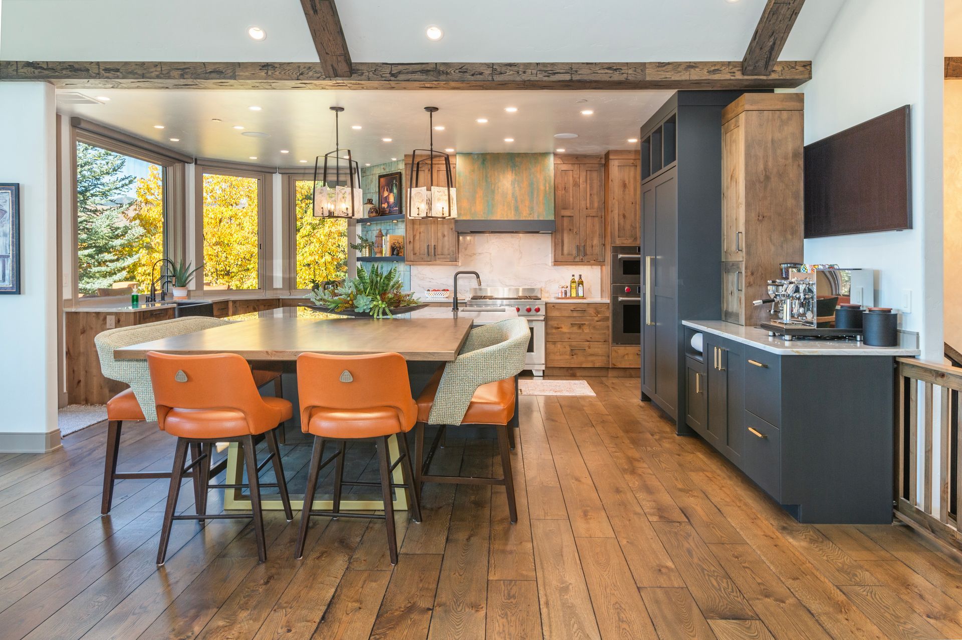 Modern open-plan kitchen with wood floors, orange chairs, island, and large windows
