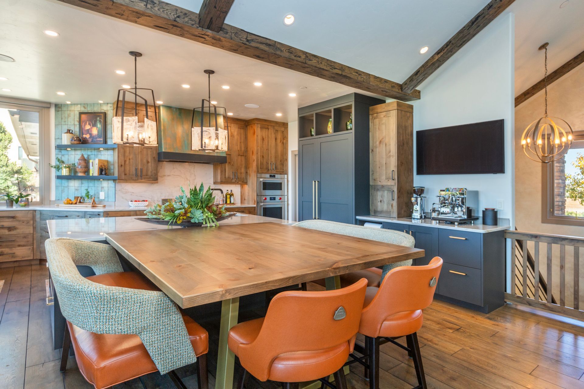 Modern kitchen and dining area with a large wooden table, orange chairs, and warm pendant lighting.