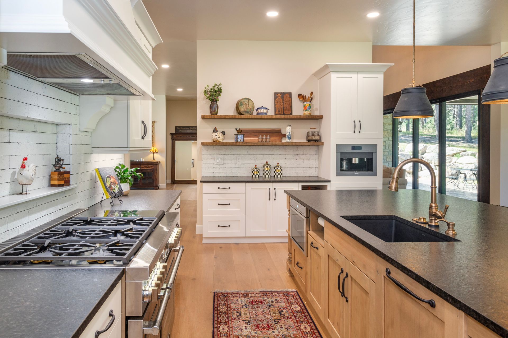 Modern kitchen with white cabinets, black countertops, gas stove, island, and large window.