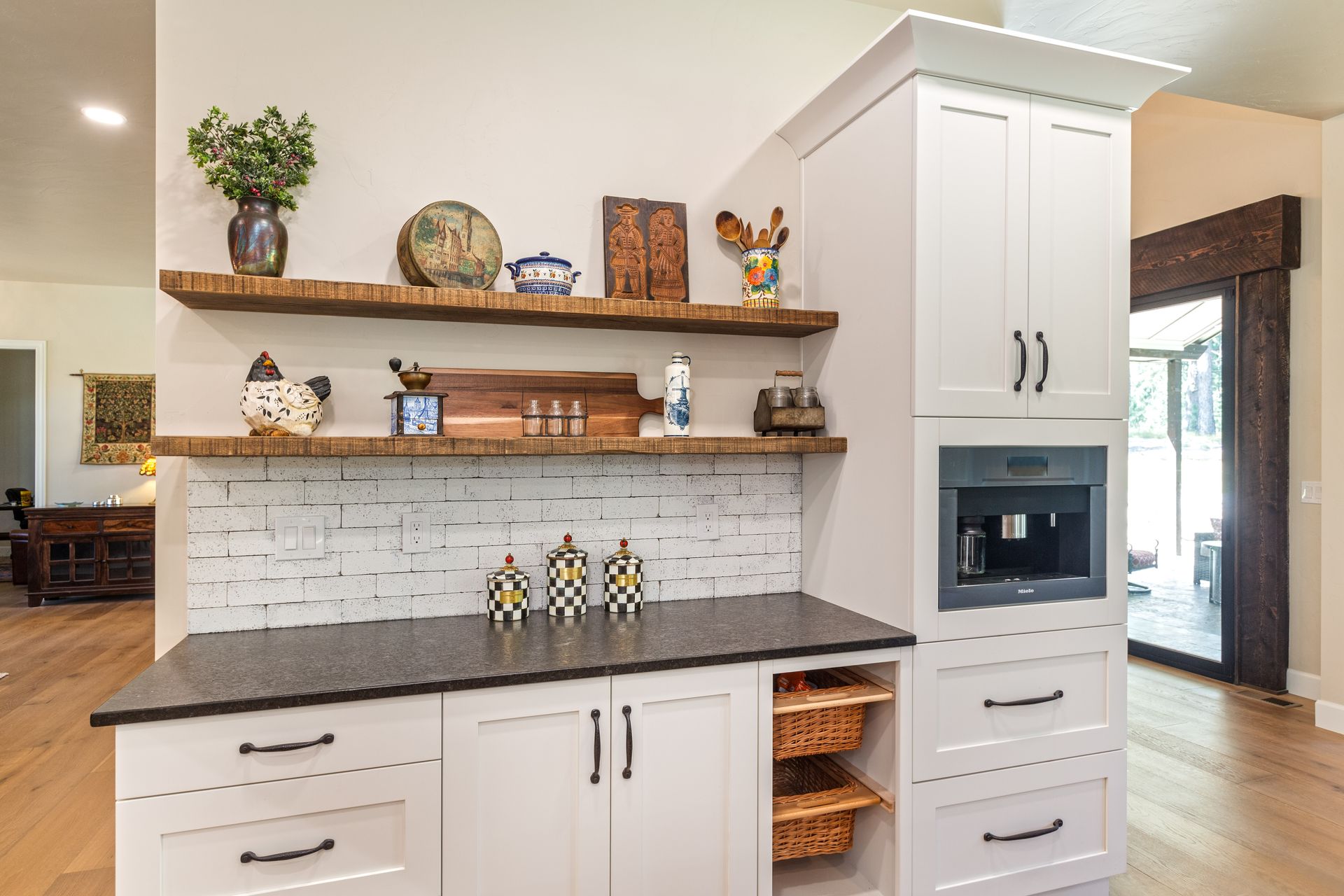 Bright kitchen coffee bar with white cabinets, dark countertop, shelves, and built-in microwave cabinet