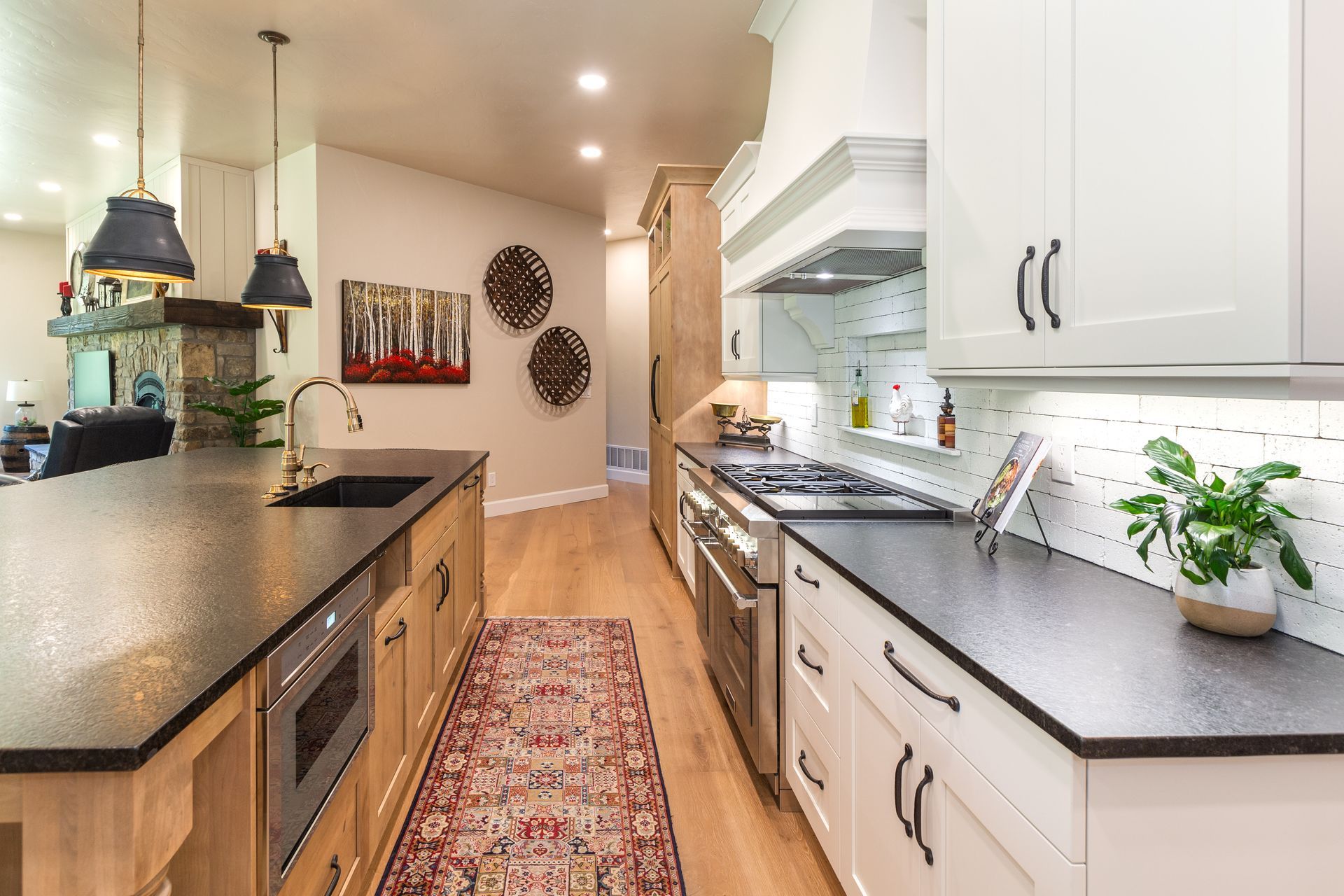 Bright modern kitchen with white cabinets, dark countertops, island, rug, and potted plants along the window.