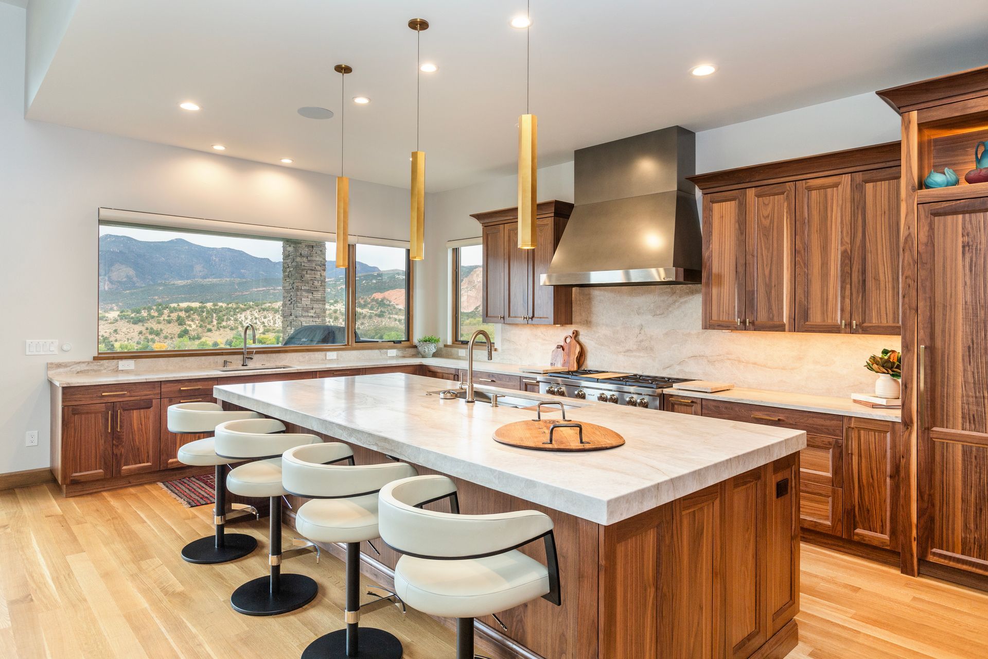 Modern kitchen with large island, pendant lights, wooden cabinets, and mountain view window
