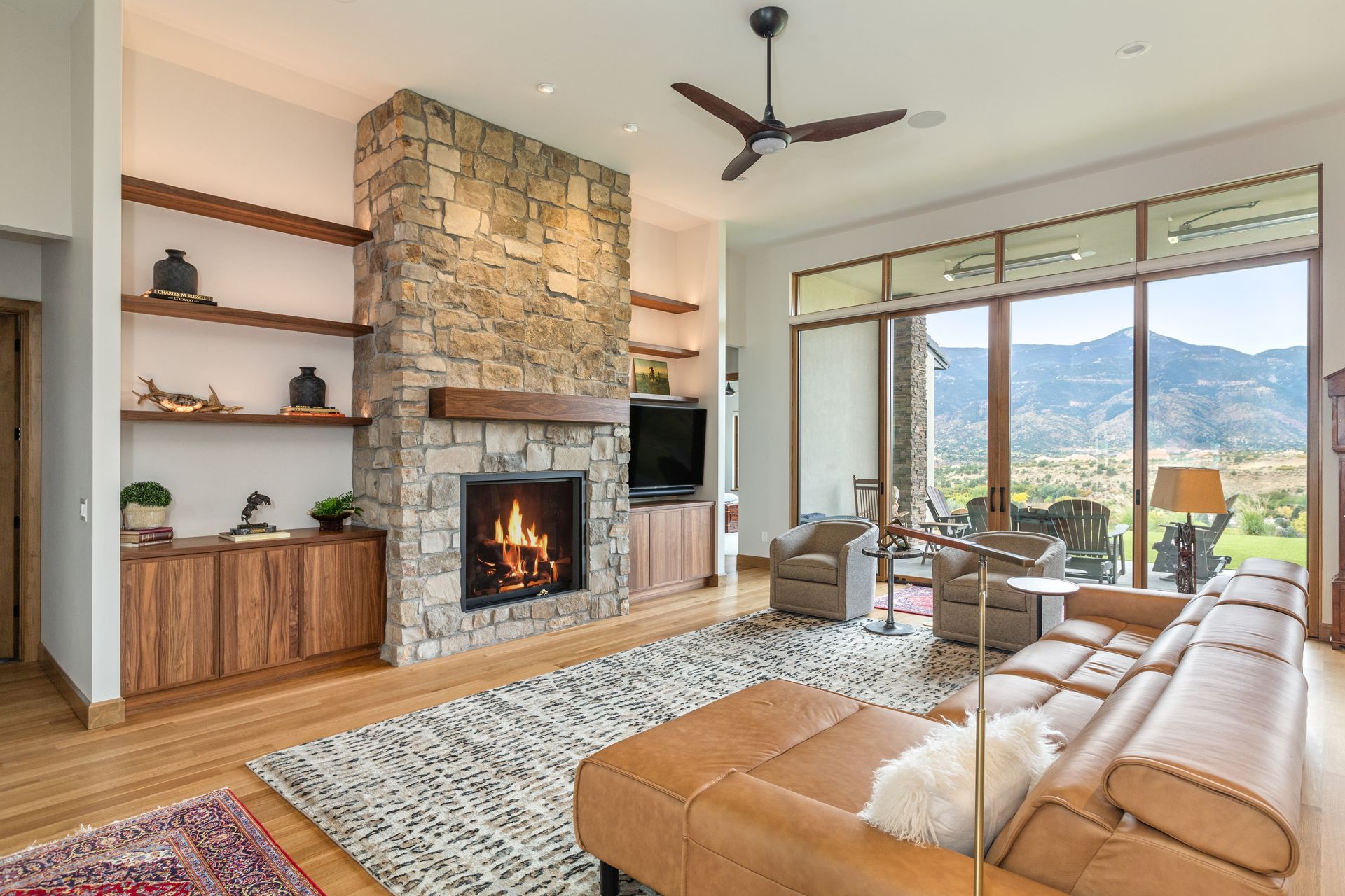 Bright living room with stone fireplace, leather sofa, rug, and mountain view through large windows