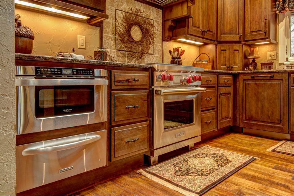 Warm wooden kitchen with stainless steel oven, cabinets, tiled backsplash, and patterned rug.