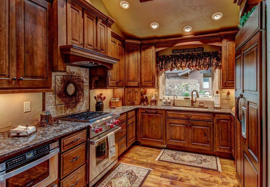 Warm kitchen with dark wood cabinets, granite countertops, stainless steel appliances, and tiled backsplash.