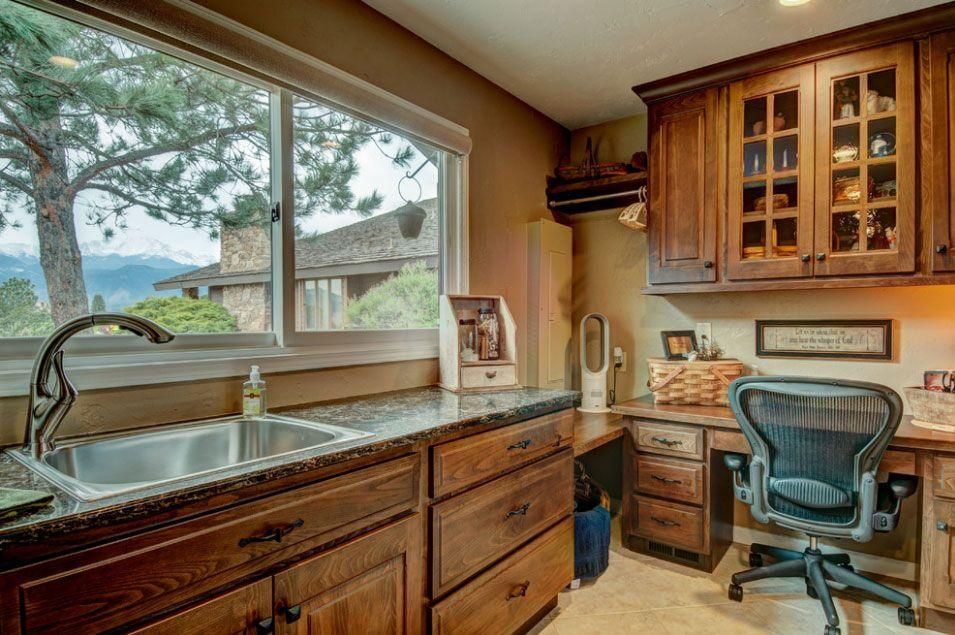 Home office with wood cabinets, desk, and large window overlooking trees and mountains