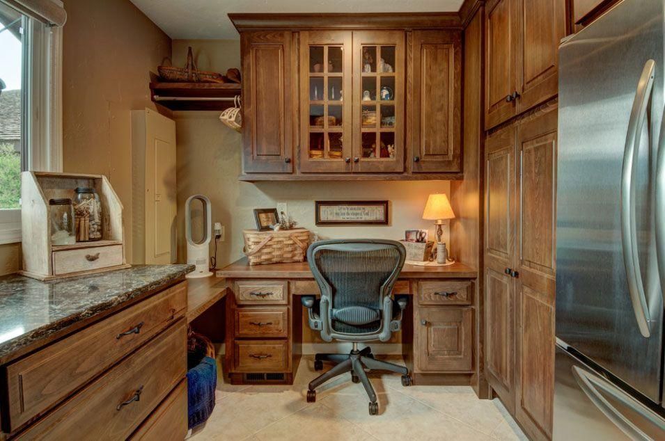 Compact home office in a kitchen, with wood cabinets, a desk chair, and a stainless steel refrigerator.