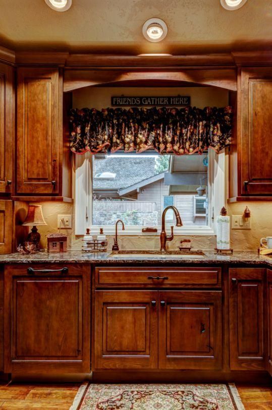 Wooden kitchen with sink beneath a window, warm lighting, and a granite countertop.
