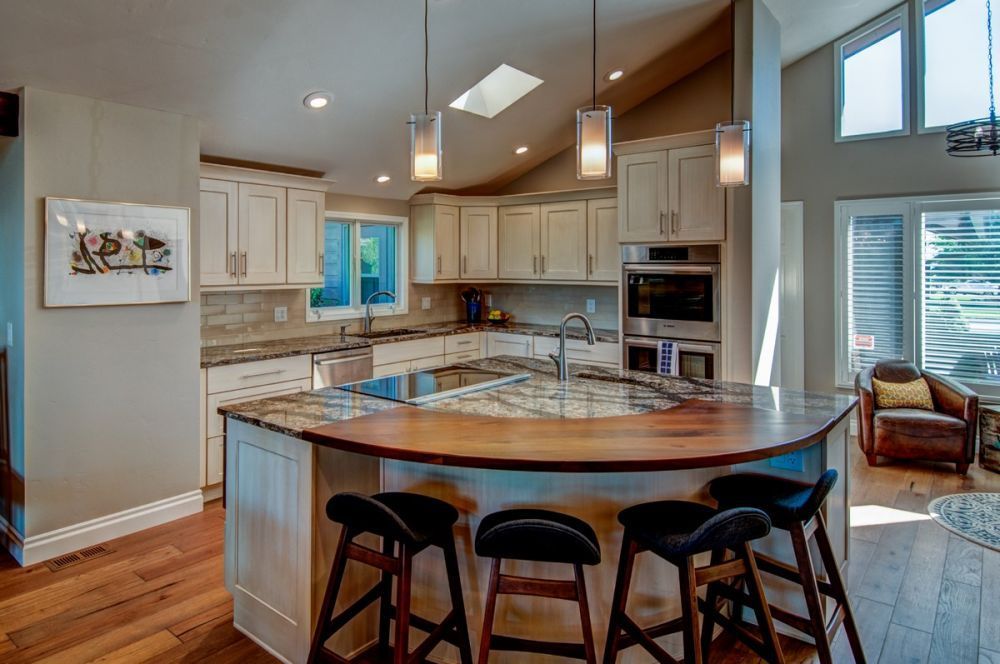 Bright kitchen with white cabinets, wood island, bar stools, and vaulted ceiling with skylights.