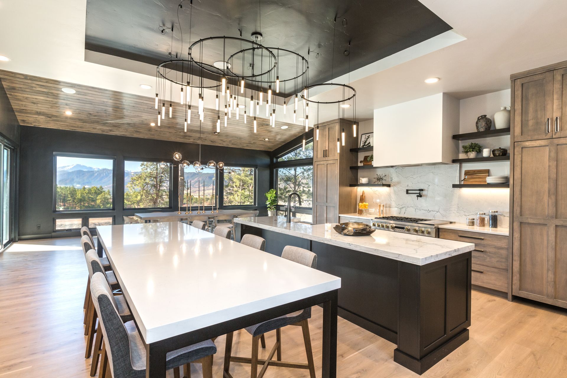 Modern kitchen with white island, dark cabinets, large windows, and pendant lights