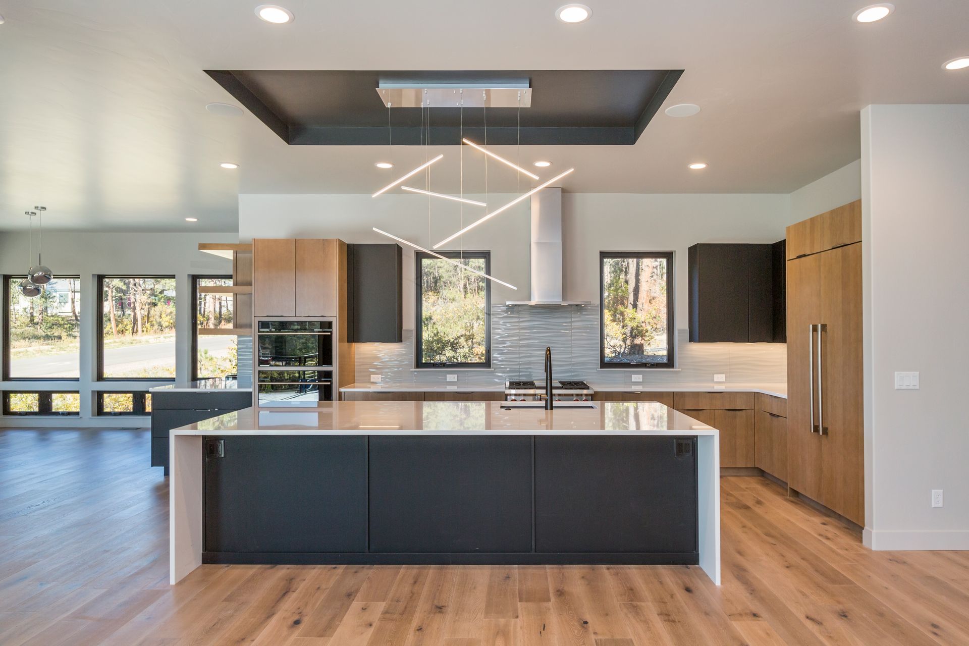 Modern open-concept kitchen with large island, white cabinets, wood floors, and black ceiling details