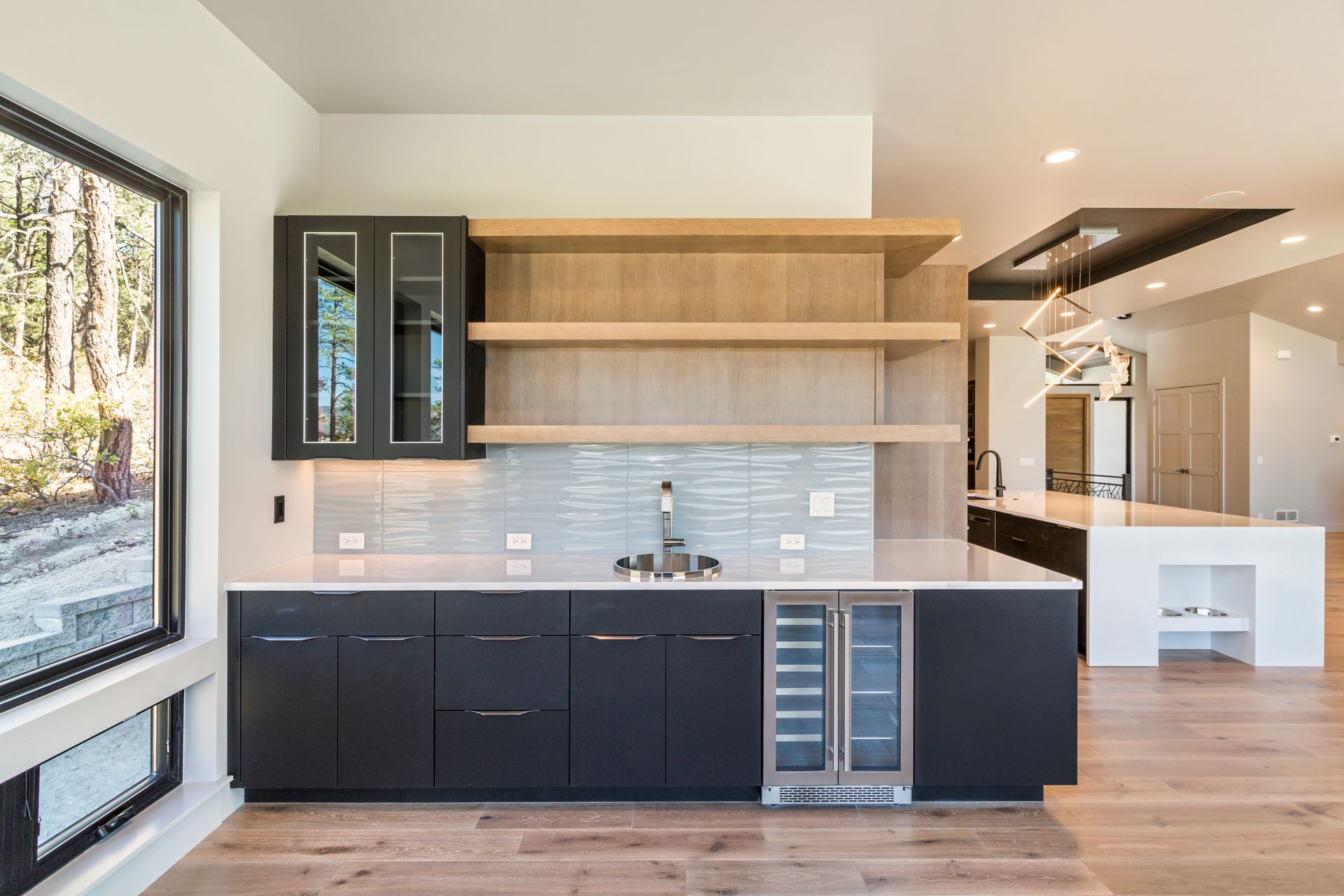 Modern kitchen with black cabinets, wood shelves, large window, and light wood floors