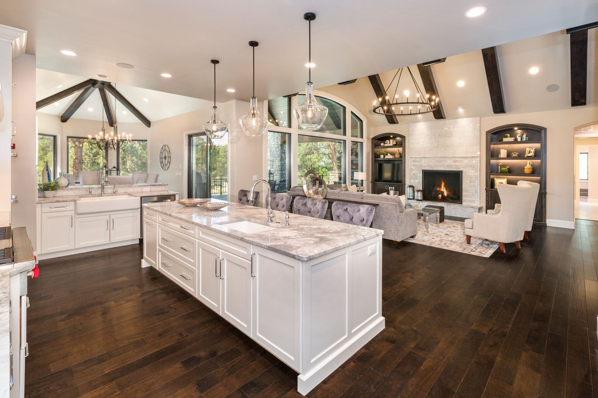Bright modern kitchen and living area with marble island, dark floors, and large windows