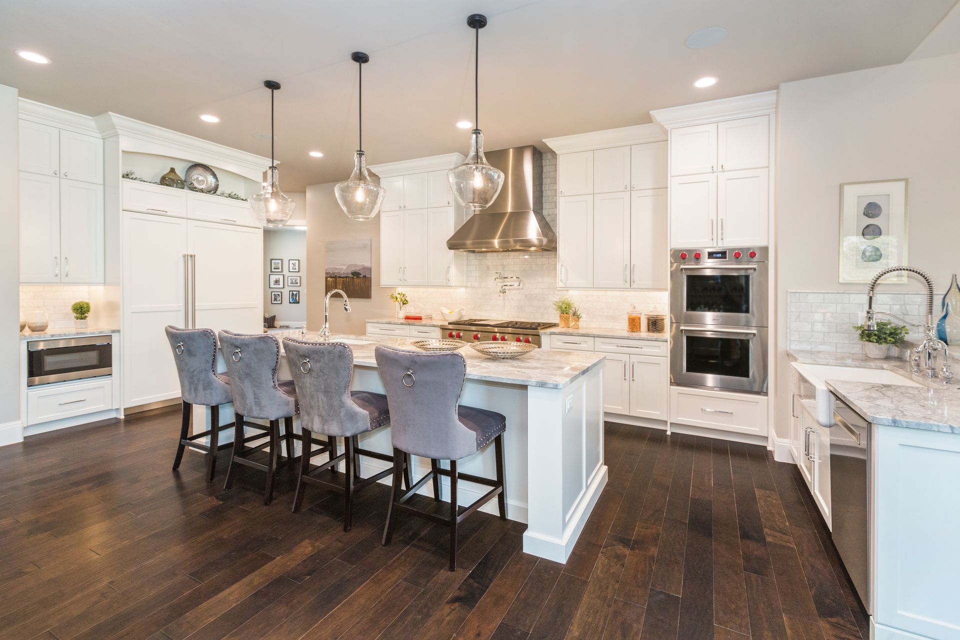 Modern white kitchen with dark wood floors, island seating, marble counters, and stainless-steel appliances