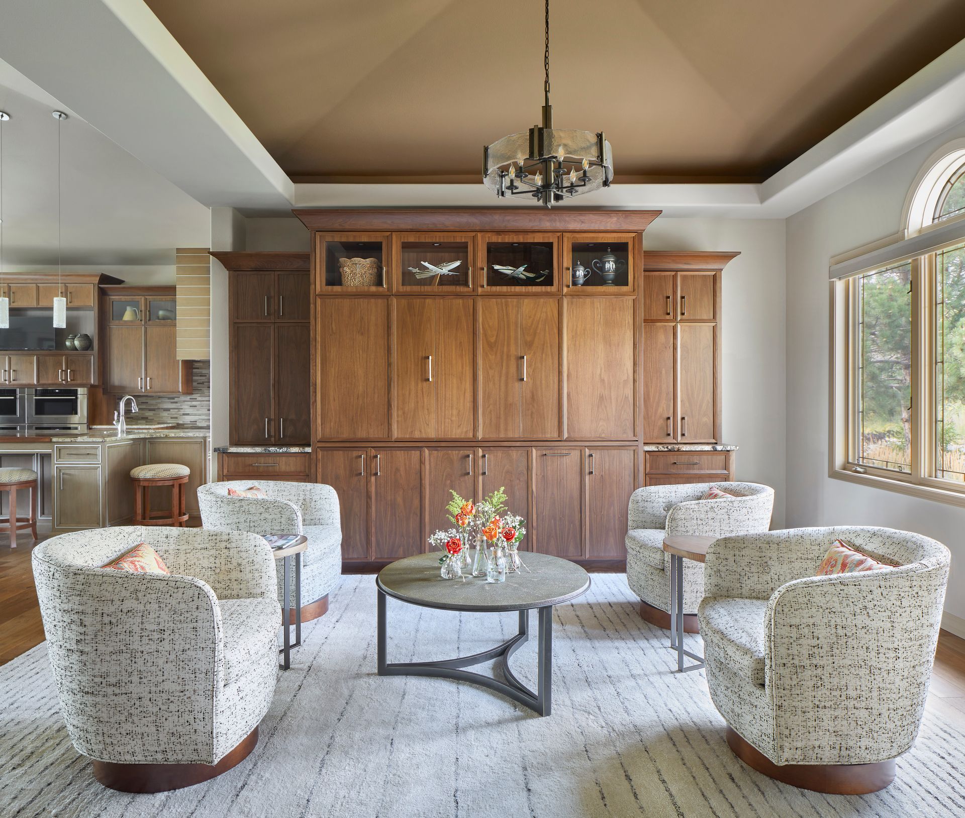 Bright living room with floral armchairs, round coffee table, and built-in wooden cabinets under a chandelier