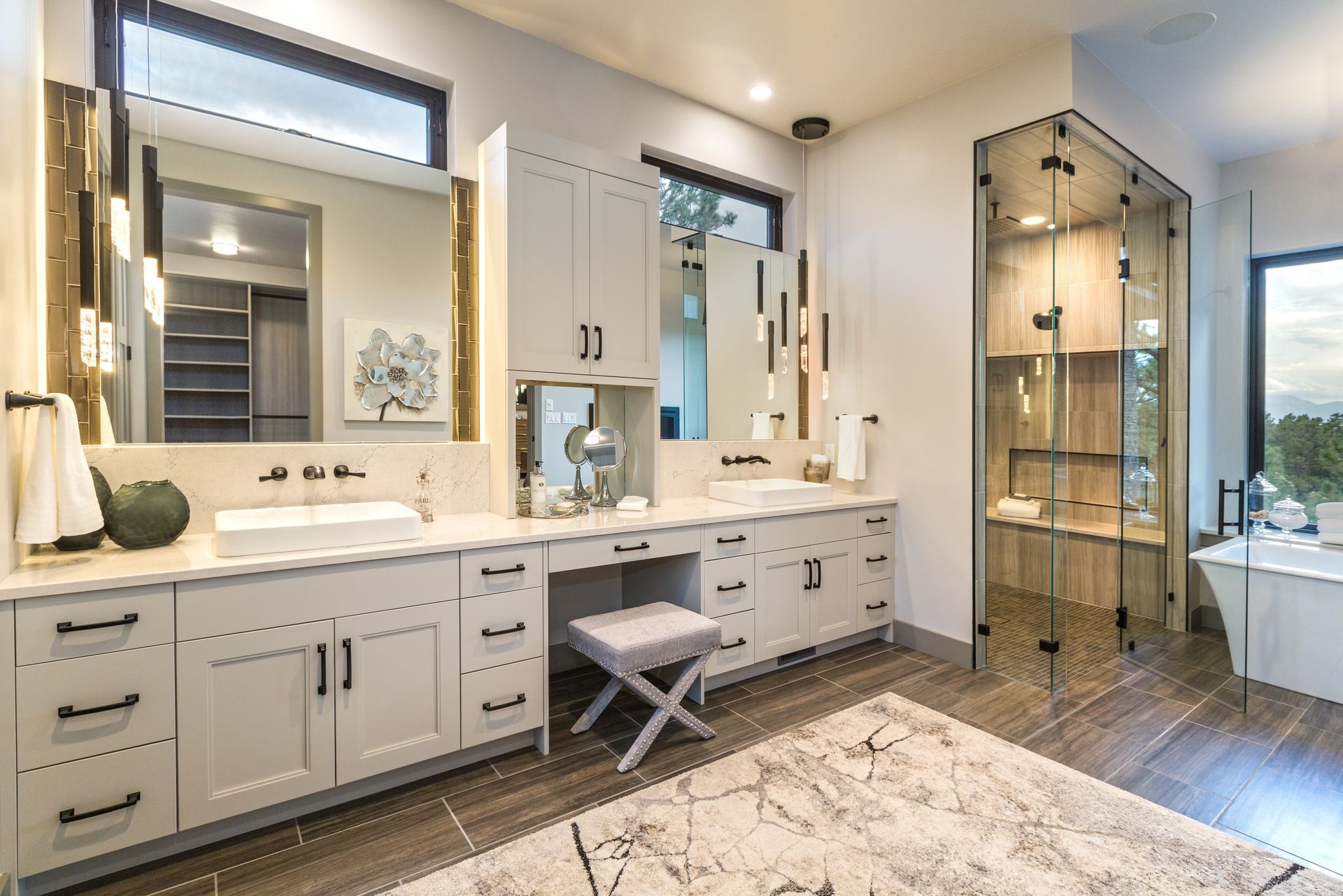 Bright modern bathroom with double vanity, large mirrors, glass shower, and wood-look floor