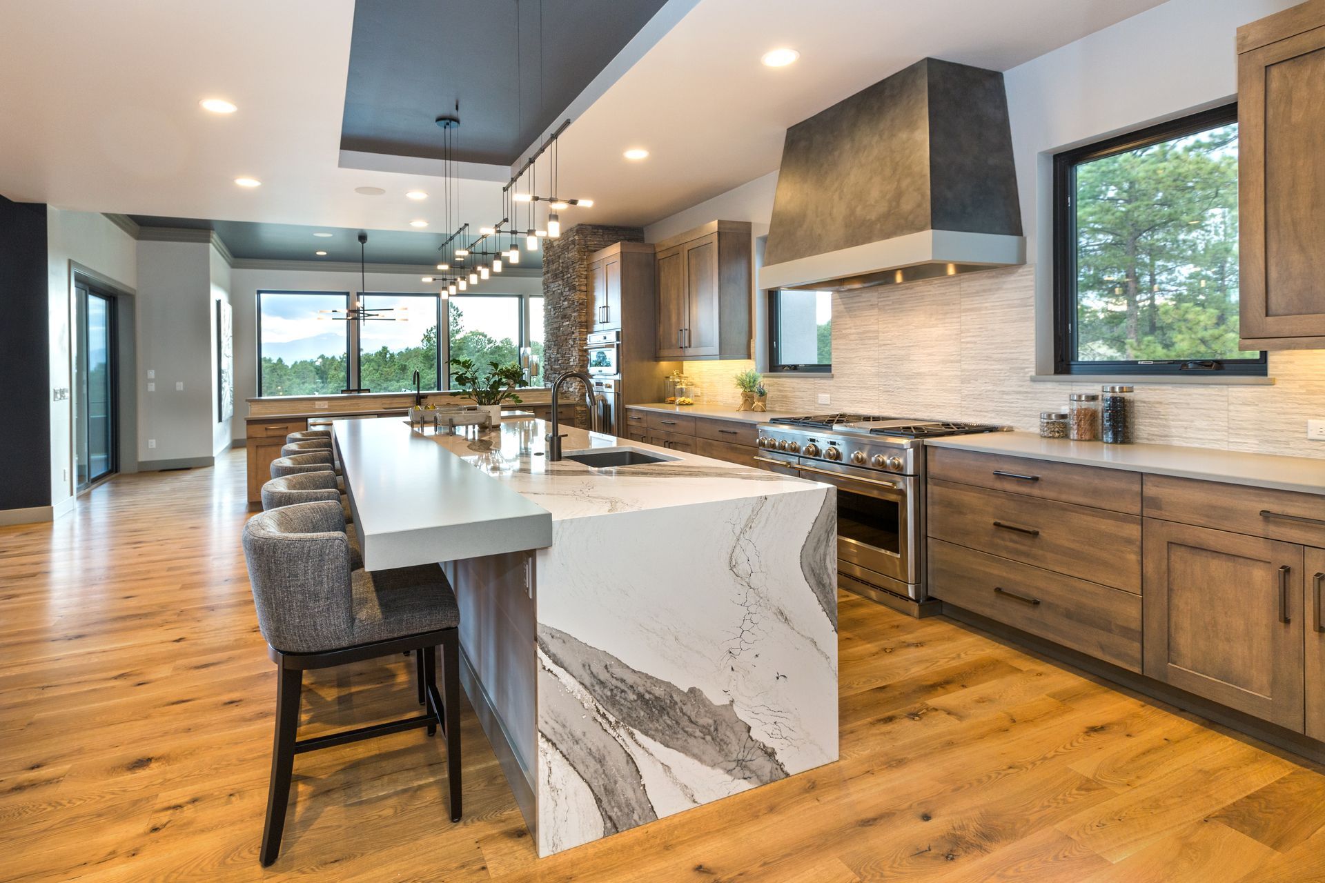 Modern kitchen with long marble island, gray cabinets, wood floors, and large windows