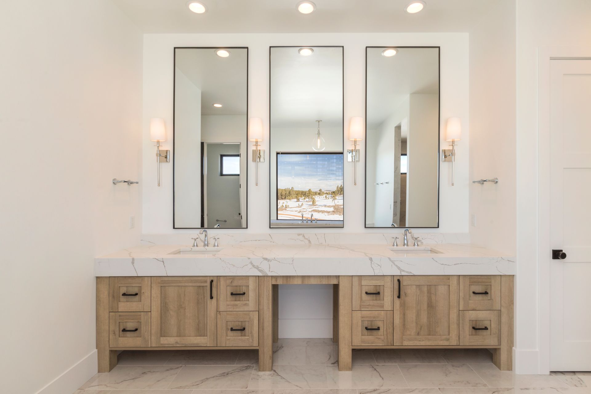 Bright bathroom vanity with double sinks, three mirrors, and light wood cabinets in a modern interior