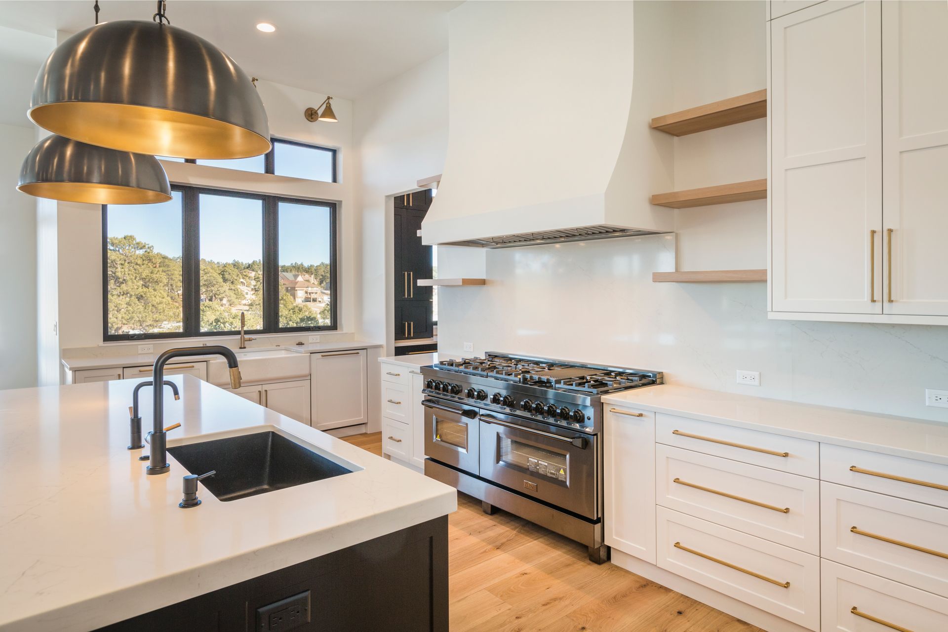 Modern white kitchen with island, brass pendant lights, gas range, and large window with mountain view