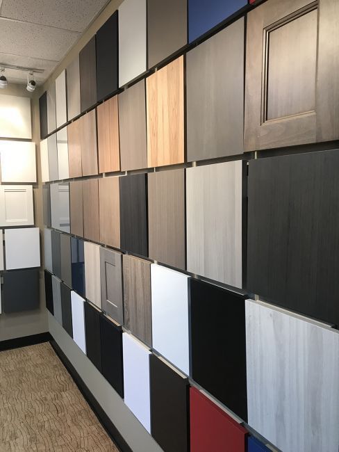 Wall of assorted cabinet door samples in a showroom, arranged in rows with neutral and wood-tone finishes