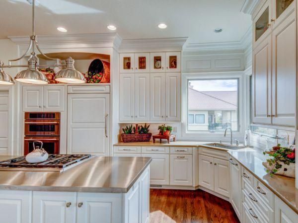 Bright white kitchen with stainless steel island, wood floors, and sunlight through a window.