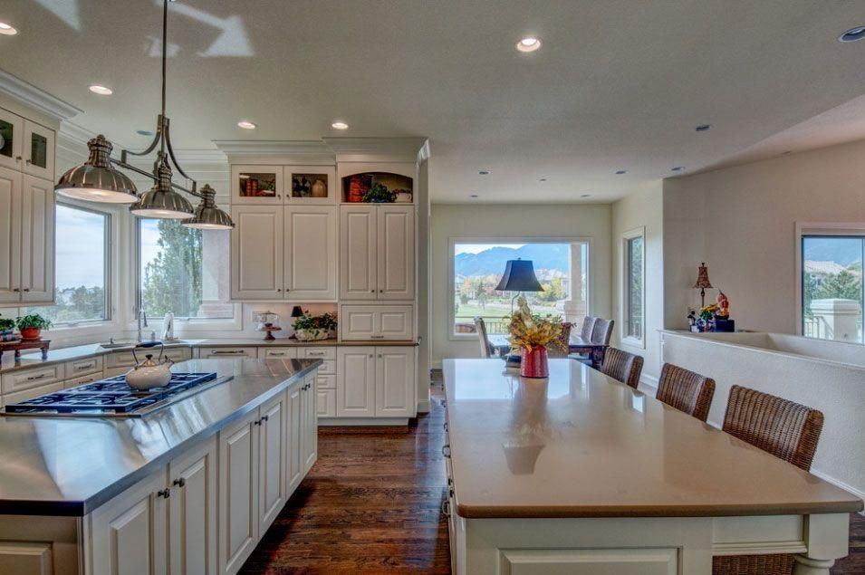 Bright modern kitchen with white cabinets, large island, and dining area by windows overlooking water.