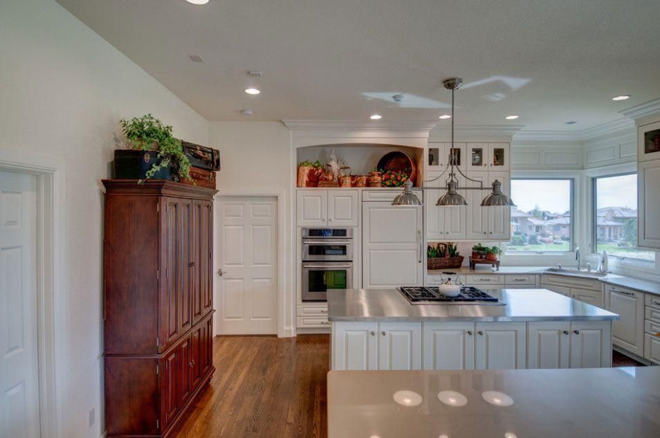 Bright modern kitchen with white cabinets, wood floors, island, pendant lights, and large windows
